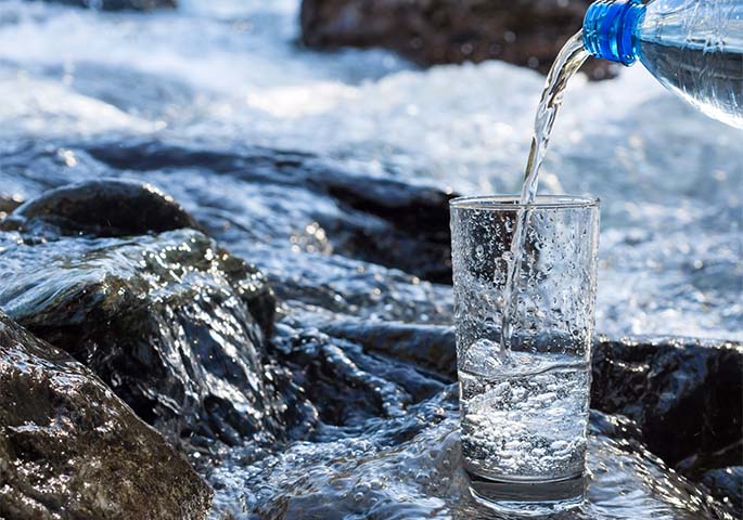 Wasserglas in welches Mineralwasser eingeschenkt wird, steht in rauschendem Fluss.