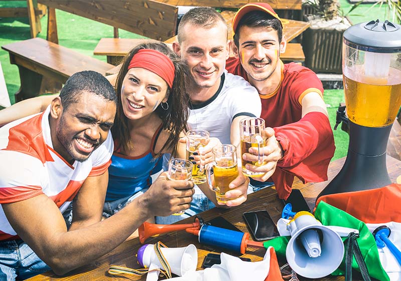 Eine Gruppe Freunde trinken zusammen Bier auf Fußballfeier mit Fanartikeln am Tisch.