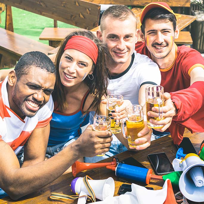 Eine Gruppe Freunde trinken zusammen Bier auf Fußballfeier mit Fanartikeln am Tisch.