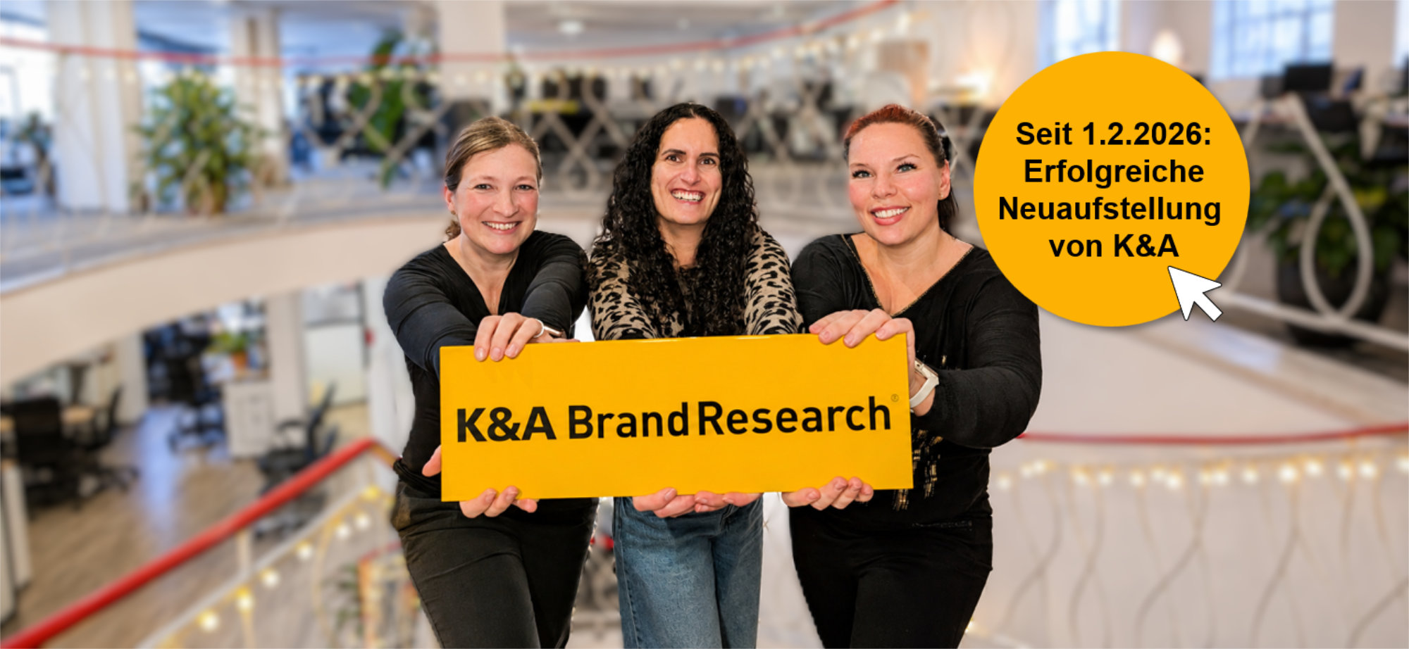Die drei Gründerinnen der K&A BrandResearch GmbH, Anja Postler, Irena Leuthold und Christina Kisskalt halten zusammen ein gelbes Schild auf dem K&A BrandResearch steht. Büro im Hintergrund und ein gelber Button mit Text "Seit 01.02.2026: Erfolgreiche Neuaufstellung von K&A" und einem Klickpfeil.