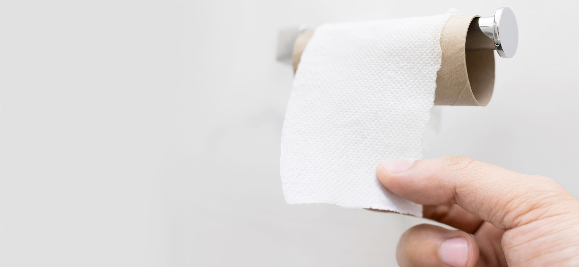 Hand unrolls last sheets from toilet paper roll.