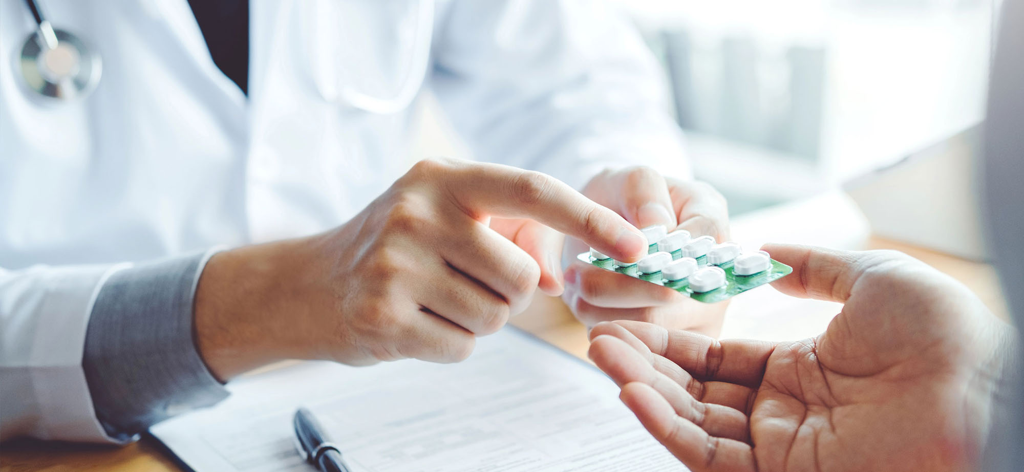 Ärztehände geben Pillenpackung an Patienten und zeigen darauf.
