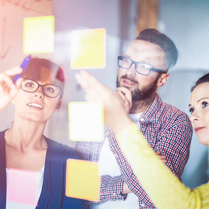 Junges Team arbeitet mit Post-Its auf Glastafel