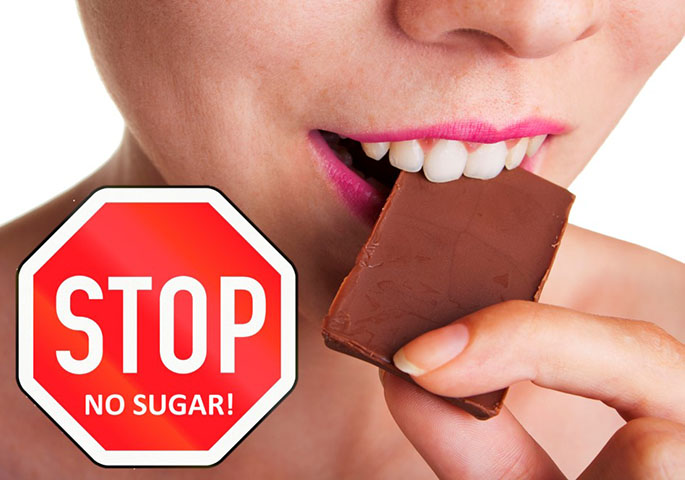 Frau beißt mit einem Lächeln in Schokolade. Daneben ein Stopschild mit der Aufschrift No Sugar.