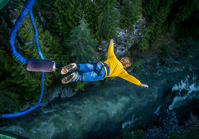 Bungee-Jumper springt mit gelbem Pullover und ausgebreiteten Armen in eine Wildwasserschlucht.