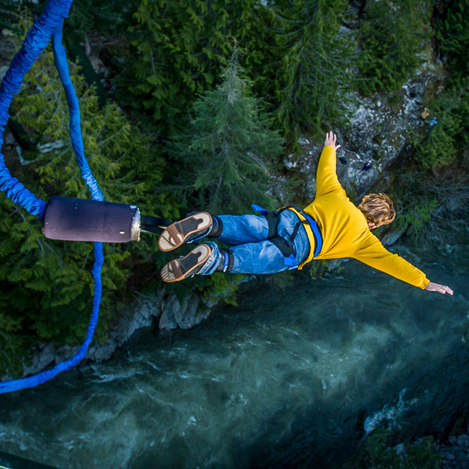 Bungee-Jumper springt mit gelbem Pullover und ausgebreiteten Armen in eine Wildwasserschlucht.