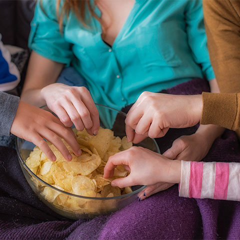 Mehrere Hände greifen in Schüssel mit Chips.
