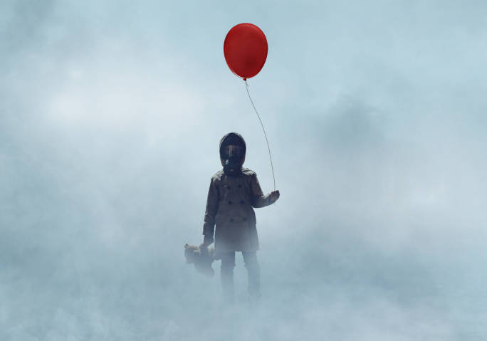 Kind mit Gasmaske steht mit rotem Ballon und Teddy in dichtem Nebel.