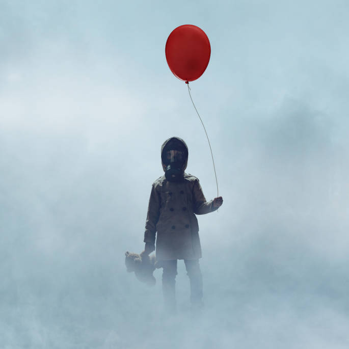 Kind mit Gasmaske steht mit rotem Ballon und Teddy in dichtem Nebel.